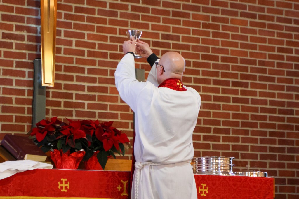 A pastor from behind holding up a communion chalice at the altar during a church service.